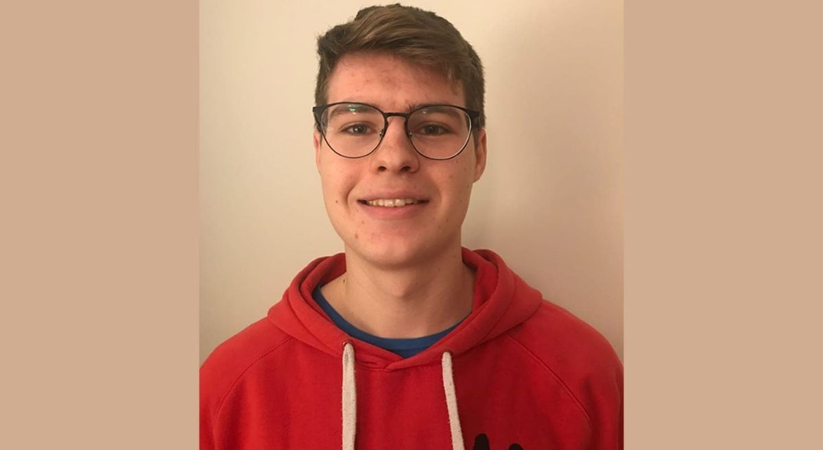 Male student, with dark hair, wearing glasses and red hoodie, smiling to camera